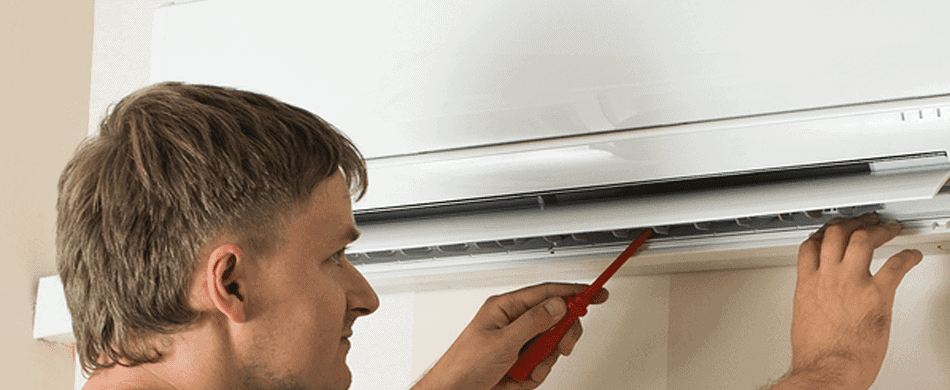 Person using a red screwdriver to adjust an air conditioner unit mounted on a wall.