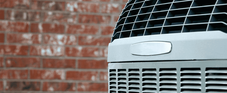 Close-up of an air conditioning unit's ventilation grille in front of a red brick wall.