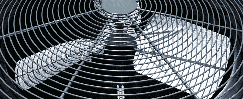 Close-up of a metal fan guard covering the blades of an industrial fan, with the blades partially visible through the grating.
