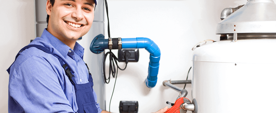 Person in work attire smiling, adjusting a valve on a large white tank with blue pipes nearby.