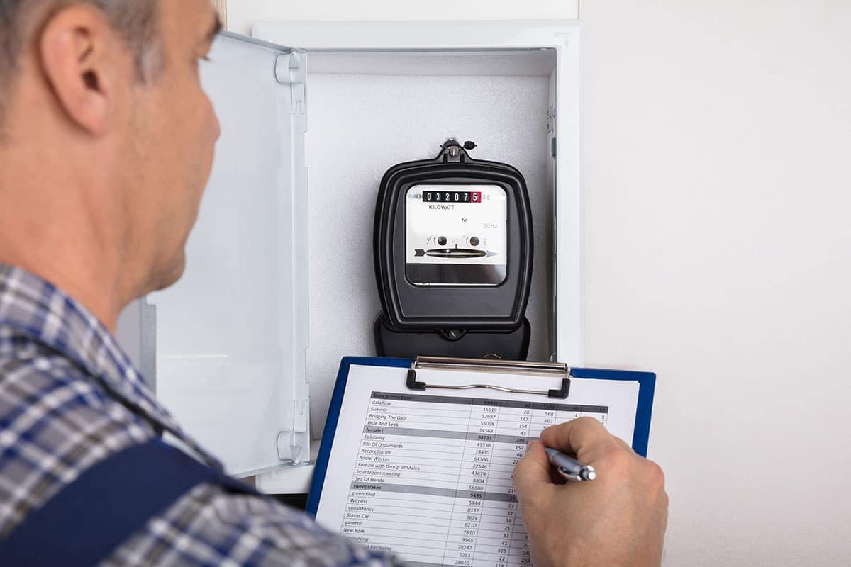 A person records data from an electricity meter into a checklist on a clipboard to monitor energy efficiency and save energy.