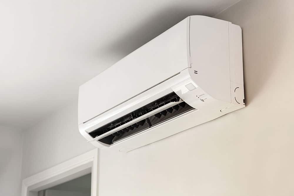 Wall-mounted white air conditioning unit installed in a room, with vents open and directed downwards.