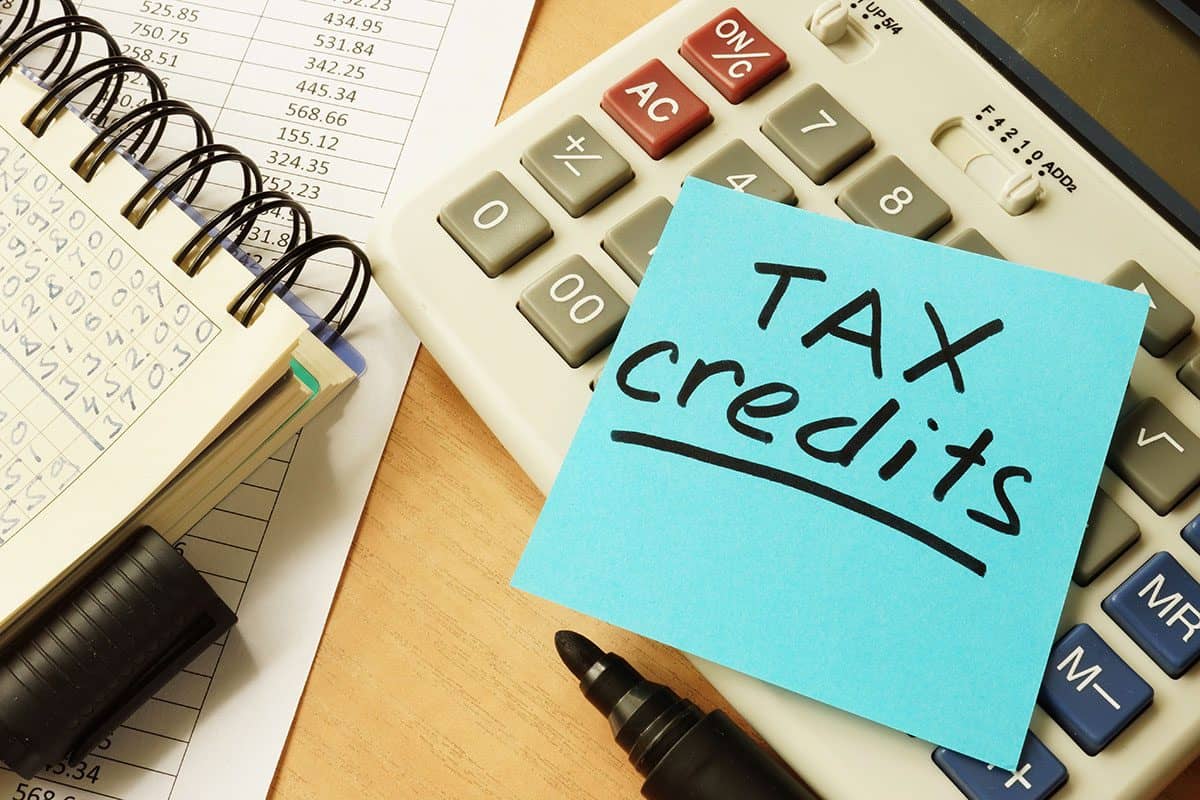 Calculator with a sticky note reading "TAX credits," a black marker, and a spreadsheet on a desk.