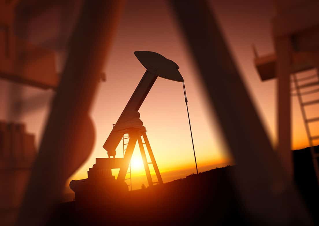 Oil pumpjack silhouette against a sunset sky, framed by blurred foreground structures.