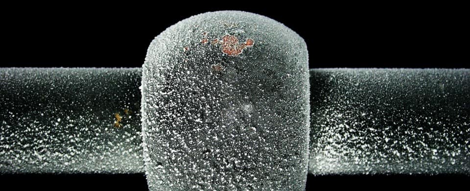 Close-up of a frost-covered metal pipe joint against a black background, highlighting texture and detail.
