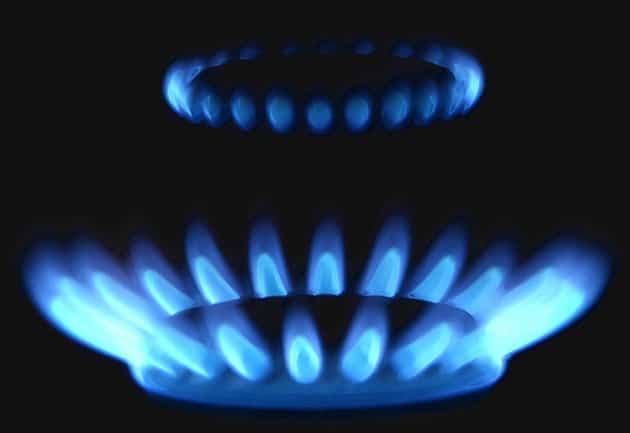 Two gas stove burners emit blue flames, illuminating the darkness with a ring shape on the back burner and a wider flame pattern on the front burner.
