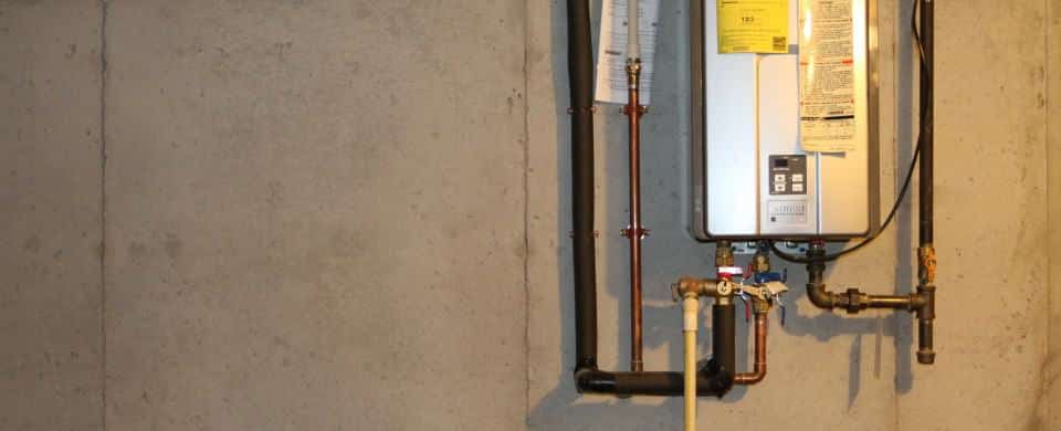 Tankless water heater mounted on a concrete wall, with visible pipes and control panel.