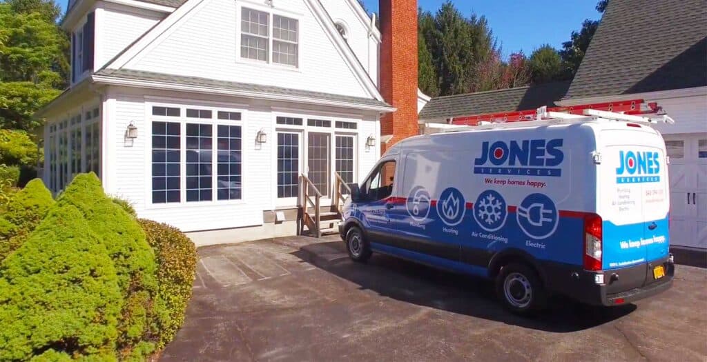 A service van with "Jones Services" logo is parked in the driveway of a white house with large windows and a prominent chimney.