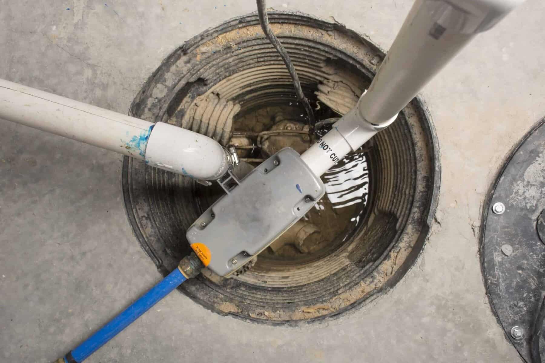 A sump pit with connected pipes and electrical wires, partially filled with water.