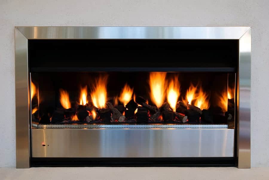 A modern, stainless steel fireplace with a rectangular frame displays a row of flames atop blackened logs.