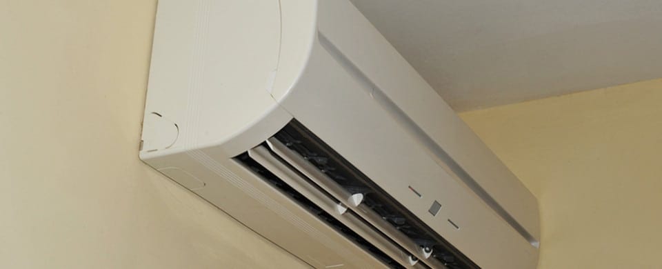 Wall-mounted air conditioning unit with an open vent, installed in a room with yellow walls.
