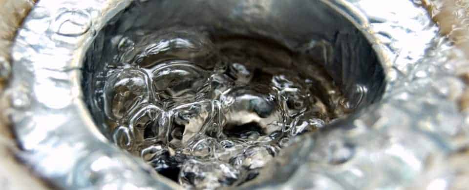 Close-up of water swirling down a stainless steel sink drain, creating a whirlpool effect.