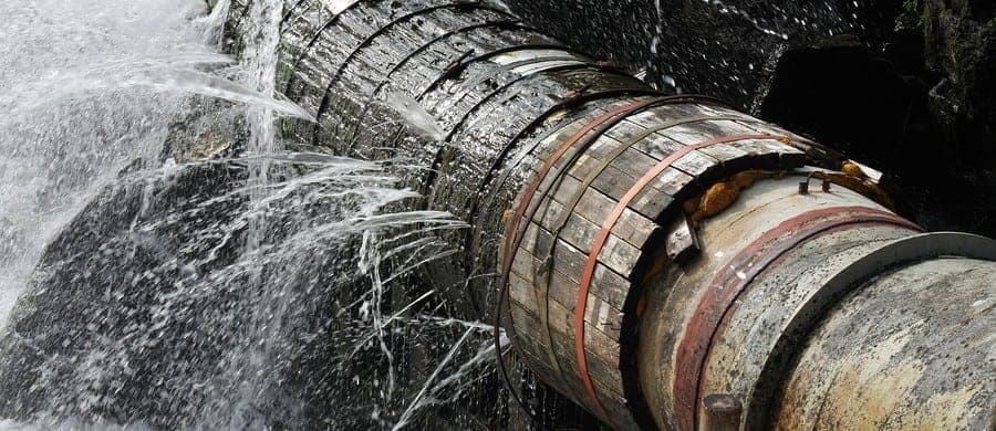 A large pipe with water leaking through gaps, surrounded by splashes, emphasizing deterioration and wear.