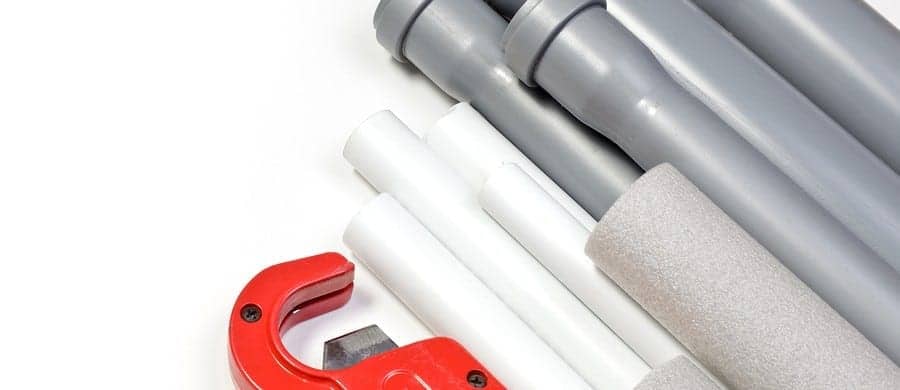 Red pipe cutter alongside several gray and white plastic pipes and foam insulation on white background.