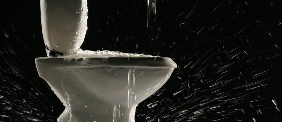 Toilet overflowing with water, splashing over the sides against a black background.