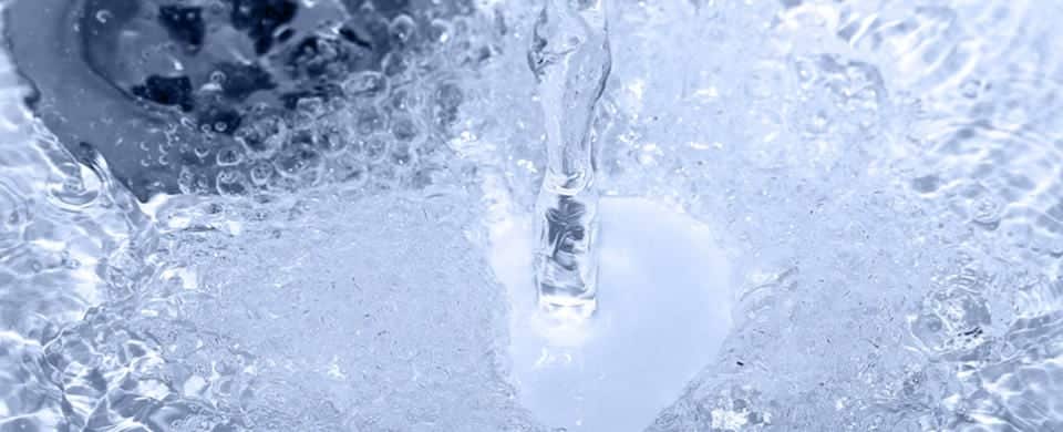 Close-up of water pouring into a sink, creating bubbles and splashes.