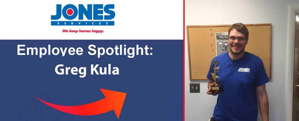 Man in a Jones Services shirt holds a trophy next to a bulletin board under a sign reading "Employee Spotlight: Greg Kula.