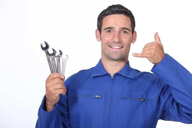 Person in a blue jumpsuit holding wrenches and making a phone gesture with their hand.