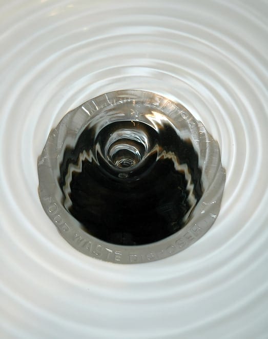 Water swirling down a sink drain, creating circular ripples around the opening.
