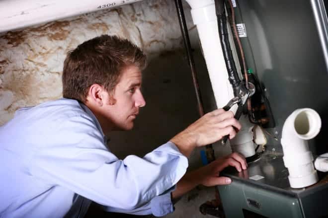 Person in a blue shirt using a wrench to adjust equipment in a dimly lit room.