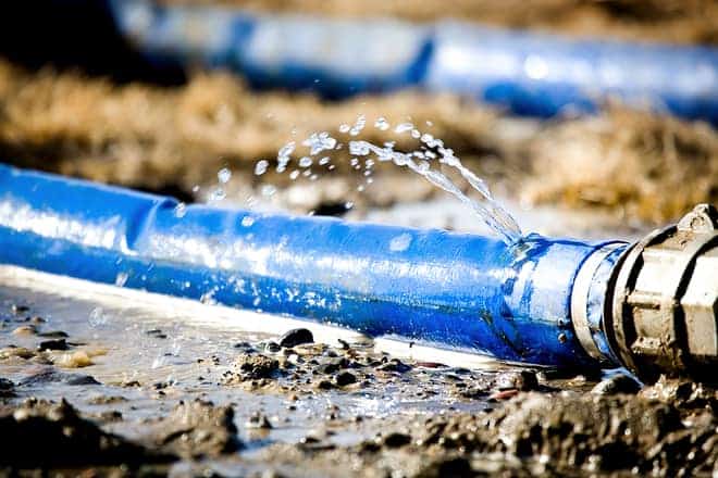 Water leaks from a blue plastic pipe lying on muddy ground.