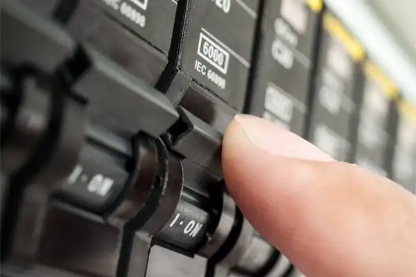 A close-up of a person's finger flipping a switch on an electrical circuit breaker panel during a routine circuit breaker service.