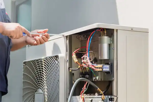 A person uses a screwdriver to repair or maintain an outdoor air conditioning unit with exposed wires and components, providing expert service in Goshen NY, similar to furnace repair.