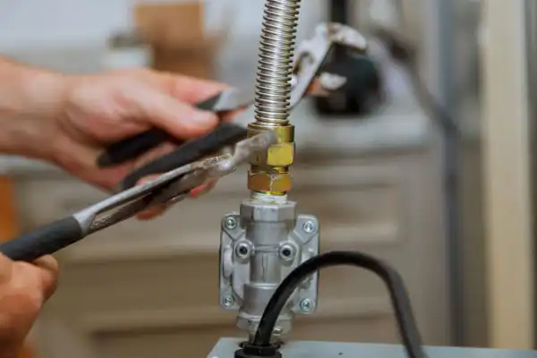 Close-up of a person using pliers to tighten a connection on a flexible gas pipe during gas line installation, working near a metal valve.
