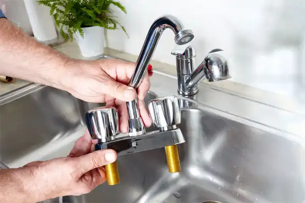 A person holds a detached kitchen faucet fixture over a stainless steel sink in Goshen NY, preparing for a kitchen plumbing installation or replacement.