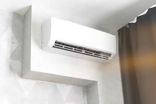 Wall-mounted air conditioner installed near the ceiling in a corner of a room, next to dark curtains and a light-colored wall—perfect for homes in Goshen NY needing Mini-Split Repair.