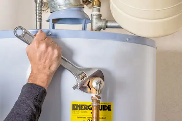 A person in Goshen NY adjusts a pipe fitting on a water heater with a large wrench. The heater has an EnergyGuide label, suggesting expert Water Heater Repair in progress.