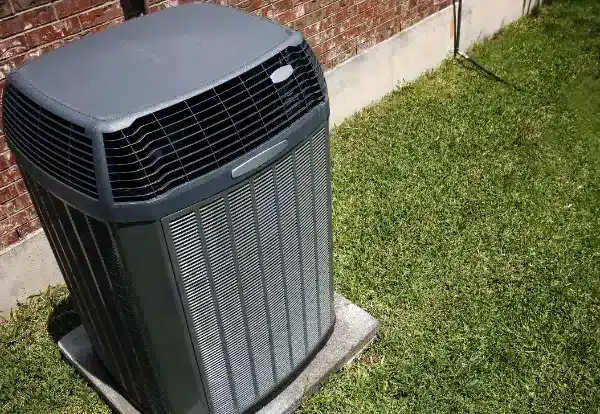 Outdoor central air conditioning unit placed on a concrete slab next to a brick exterior wall and grass lawn after expert Air Conditioning Installation in Goshen NY.