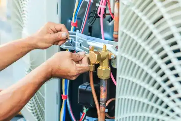 Close-up of a person performing Air Conditioning Maintenance on electrical and copper components in an HVAC unit in Goshen NY, with various wires and tools visible.