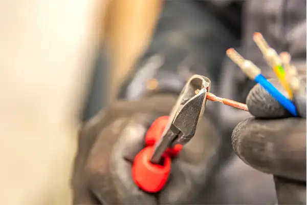 A person wearing gloves uses wire cutters to trim the end of a copper electrical wire, held among several colored wires during an electrical installation in Goshen NY.