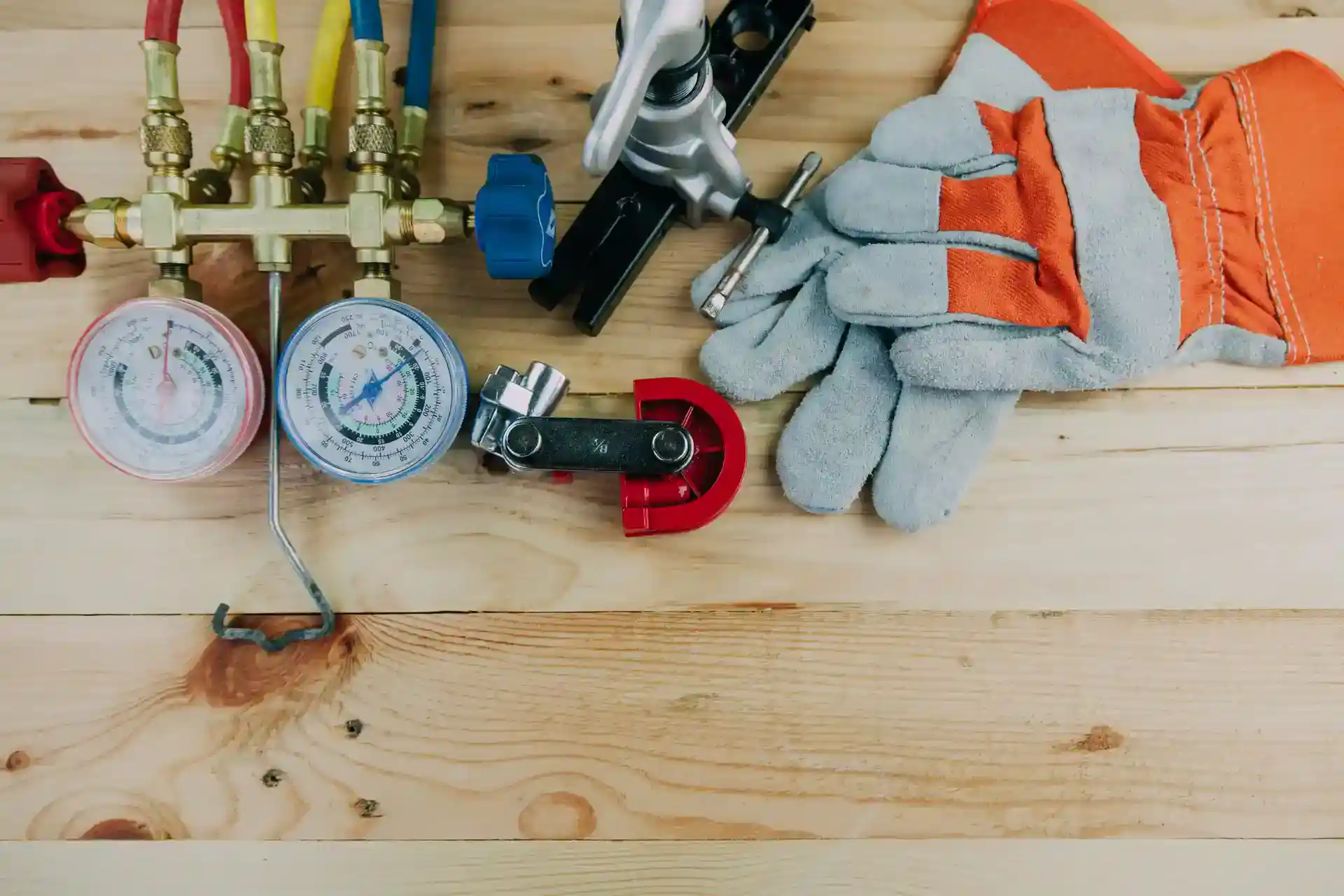 Assorted HVAC tools, including gauges, cutting tools, and protective gloves, placed on a wooden surface.